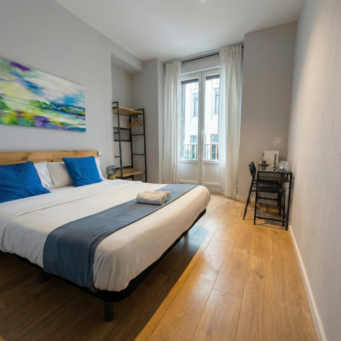 Habitaci&oacute;n moderna con cama doble, escritorio y ventanal luminoso.