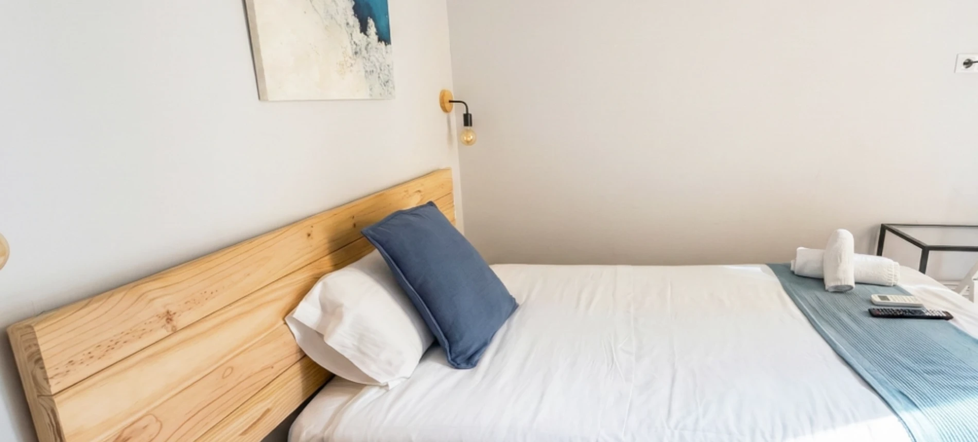 Cama con cabecera de madera, cojines azules y mesita en habitaci&oacute;n sencilla.
