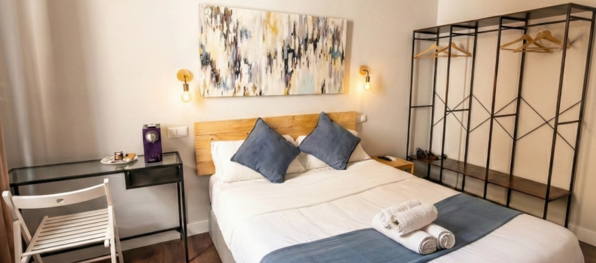 Habitaci&oacute;n moderna con cama doble, escritorio y perchero minimalista.