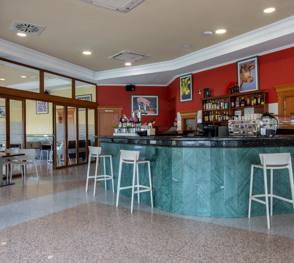 Bar con mostrador verde, sillas blancas y decoraci&oacute;n colorida en las paredes.