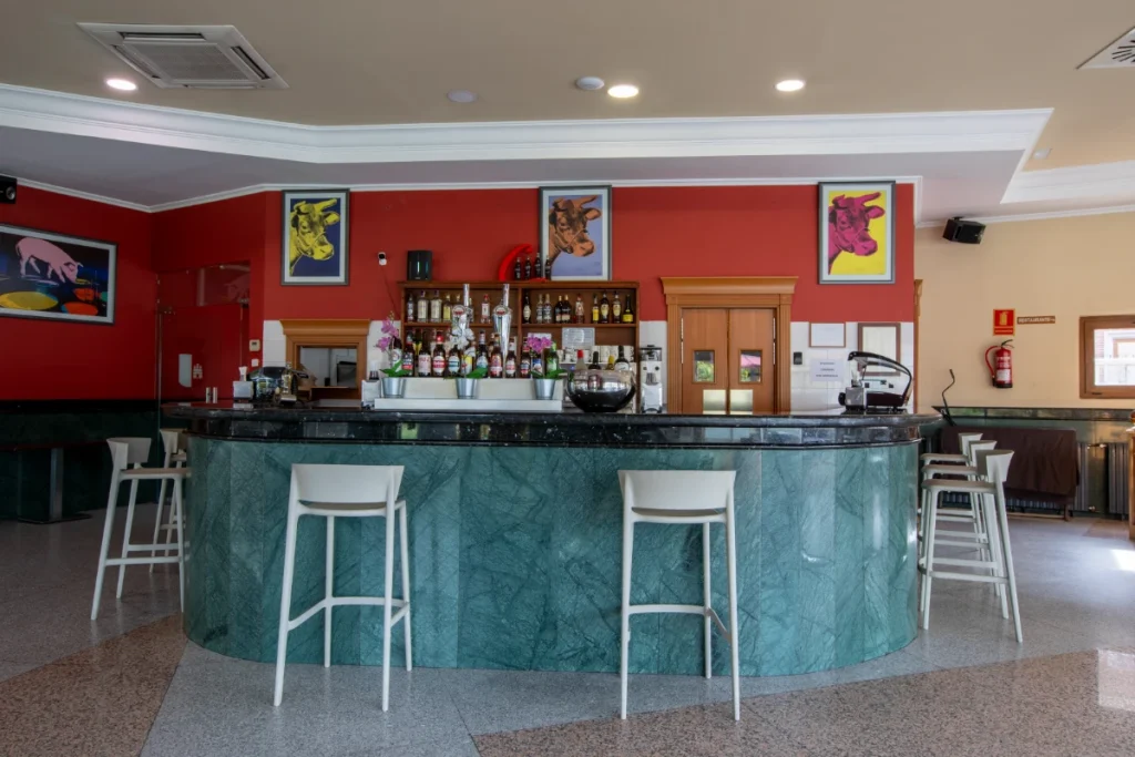 Bar con barra curva, sillas blancas y paredes rojas decoradas con arte pop.