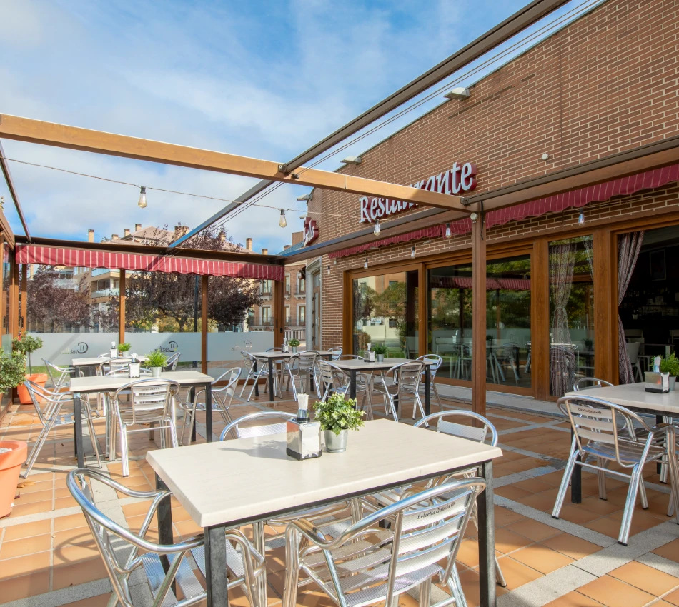 Terraza de restaurante con mesas y sillas met&aacute;licas bajo un cielo despejado.