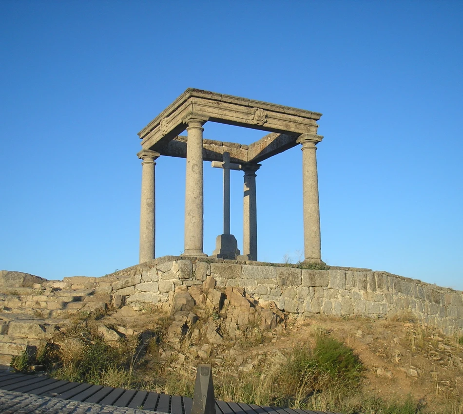 Templo romano de piedra con columnas y cruz bajo un cielo azul.