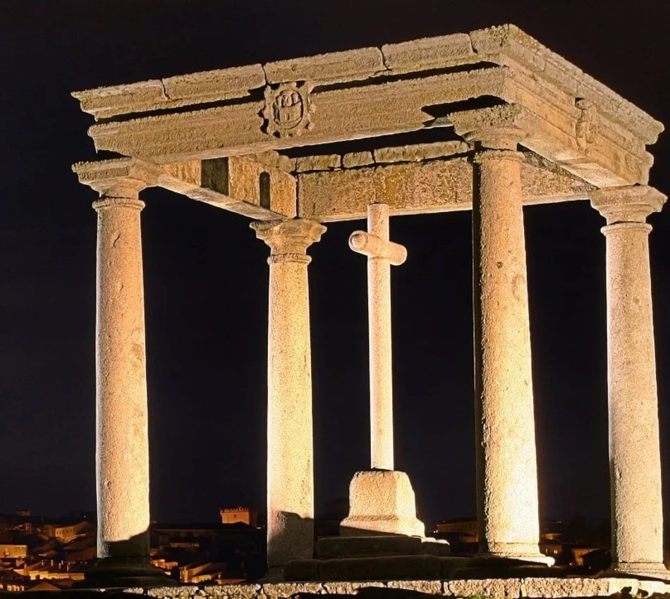 Arco de piedra iluminado en la noche con cruz en el centro.