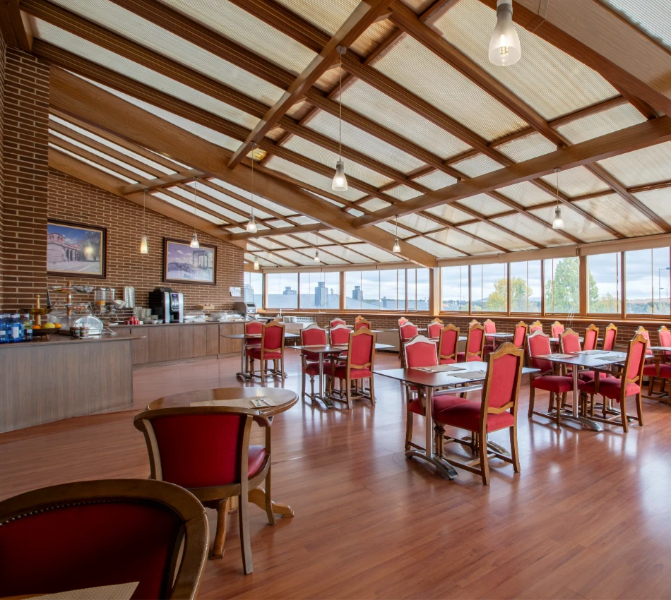 Comedor elegante con techo de vigas y sillas rojas cerca de ventanales amplios.