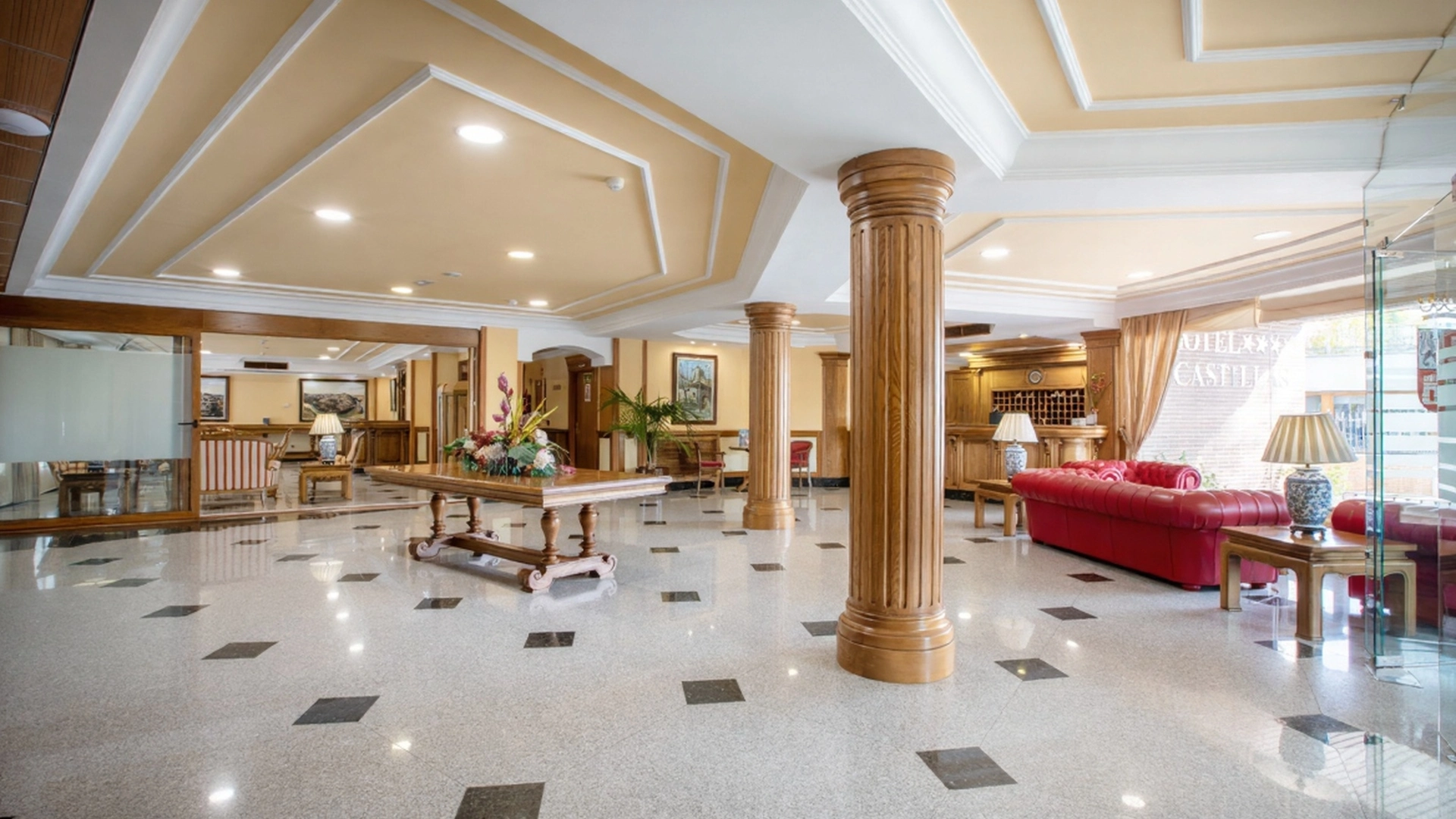 Vest&iacute;bulo de hotel elegante con columnas de madera y muebles cl&aacute;sicos.