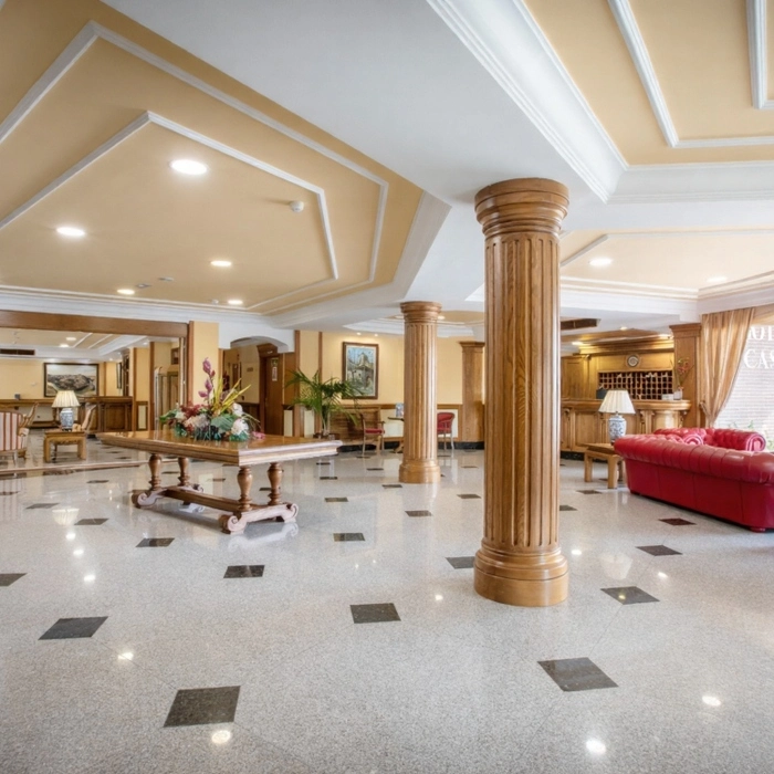 Vest&iacute;bulo de hotel elegante con columnas de madera y muebles cl&aacute;sicos.