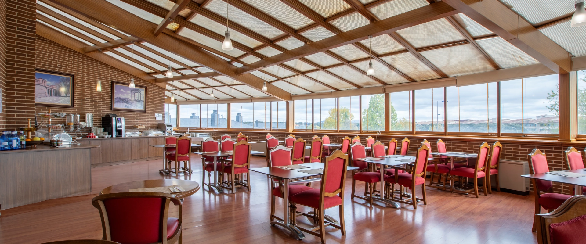 Comedor amplio con sillas rojas y mesas, decoraci&oacute;n de ladrillo y techos de madera.