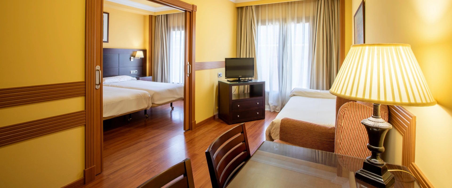 Habitaci&oacute;n de hotel con dos camas, televisi&oacute;n y l&aacute;mpara de mesa.