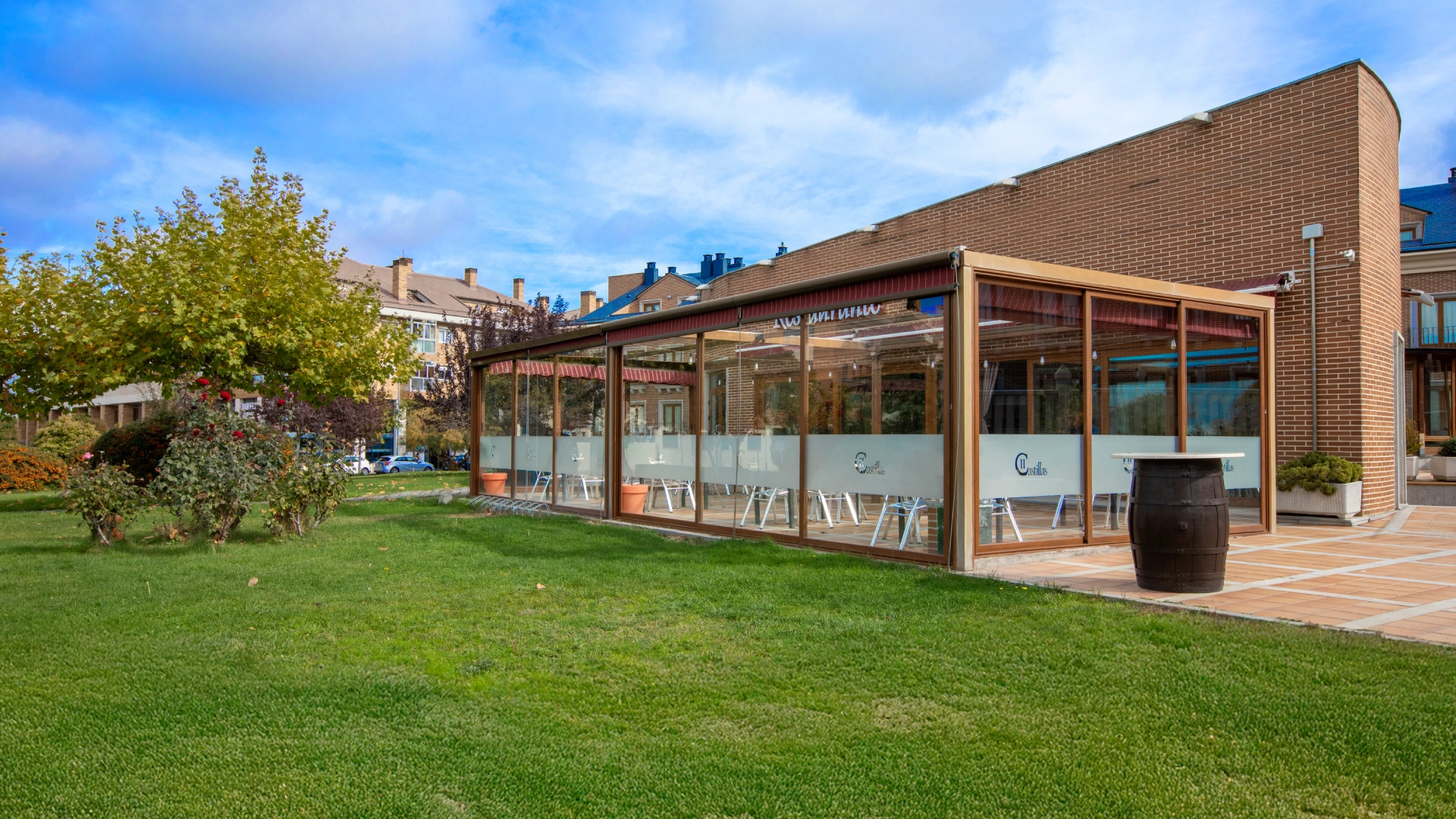 Terraza con paredes de vidrio junto a &aacute;rea verde en entorno urbano.