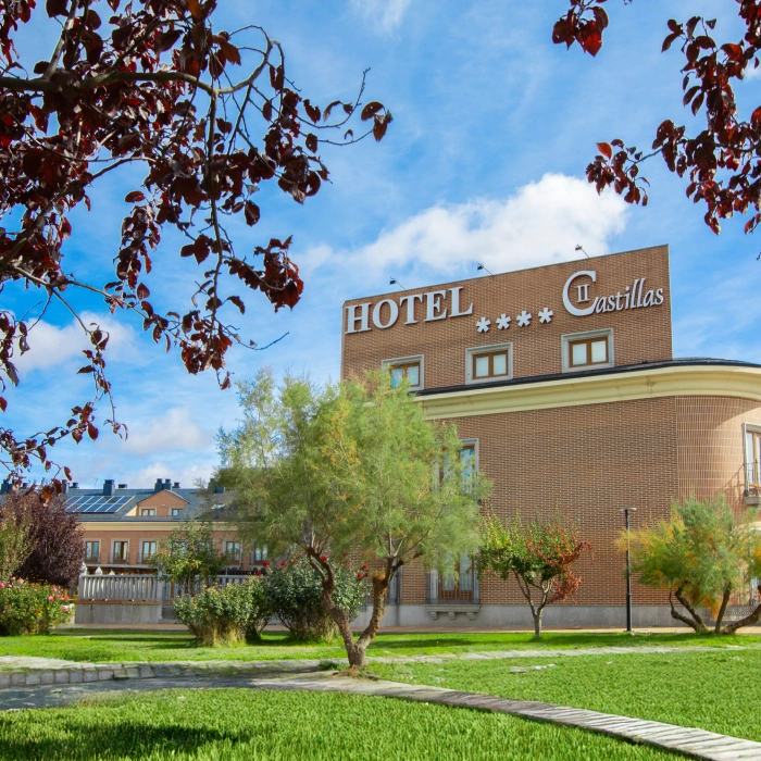 Hotel rodeado de &aacute;rboles, cielo azul y c&eacute;sped verde.