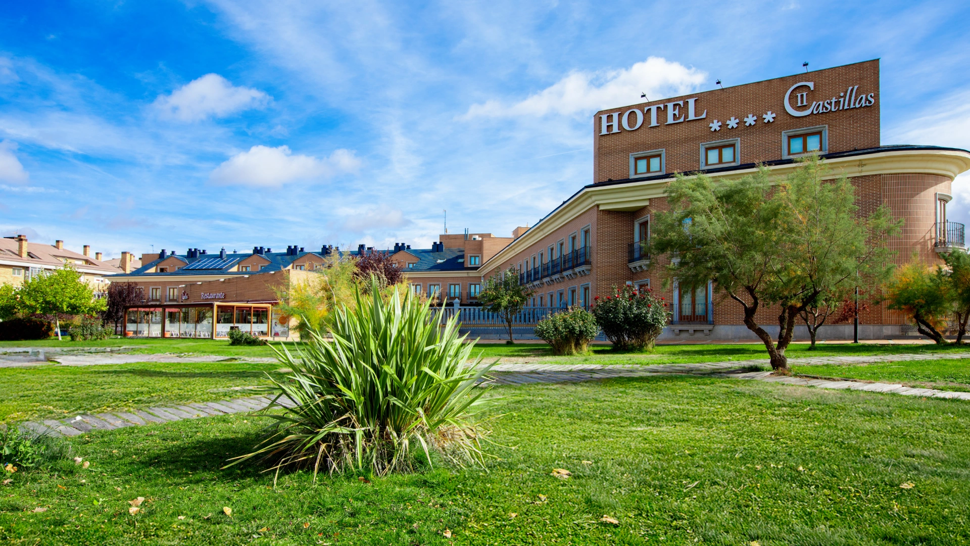 Hotel de ladrillo con jard&iacute;n en d&iacute;a soleado.
