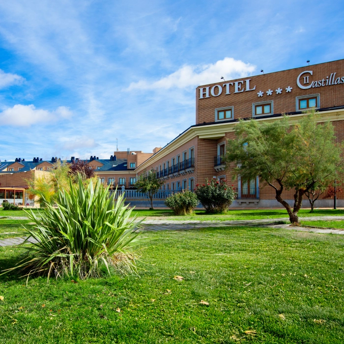 Hotel de ladrillo en un jard&iacute;n verde bajo un cielo azul con algunas nubes.