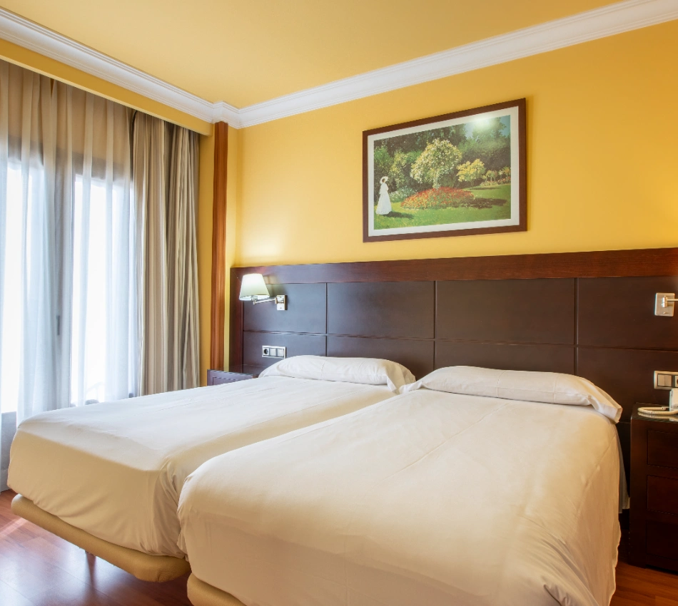 Dos camas individuales en habitaci&oacute;n de hotel con paredes amarillas y cuadro.