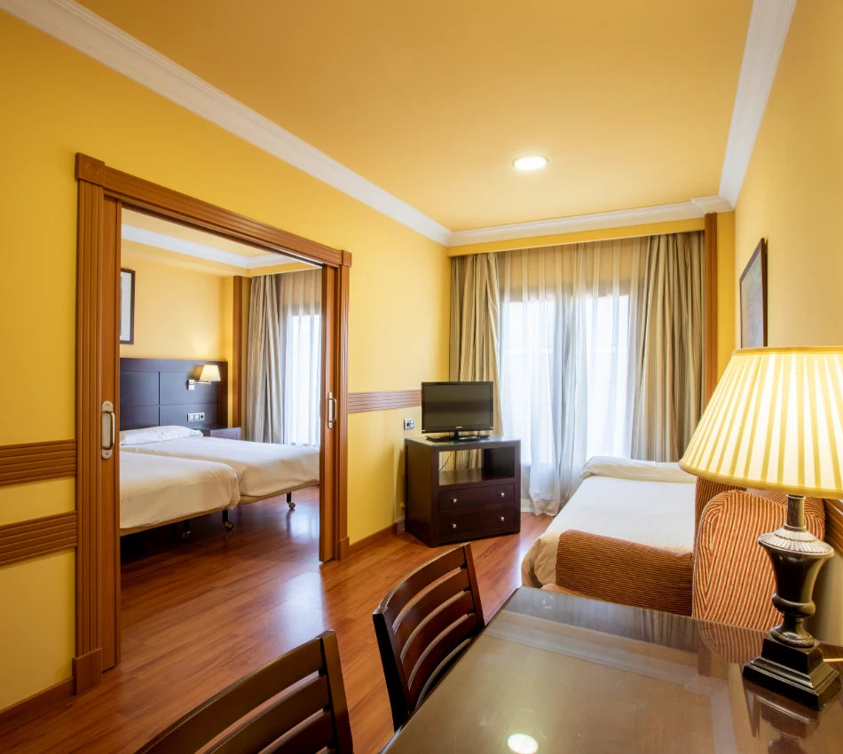 Habitaci&oacute;n de hotel con dos camas, mesa y televisor, decorada en tonos c&aacute;lidos.