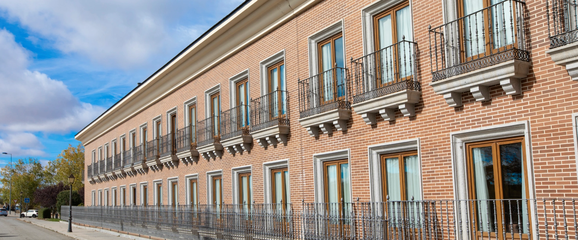 Edificio de ladrillo con ventanas y balcones, cielo azul al fondo.