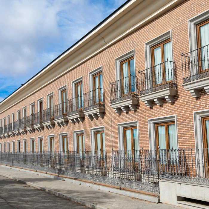 Edificio de ladrillo con ventanas y balcones en una calle con cielo despejado.