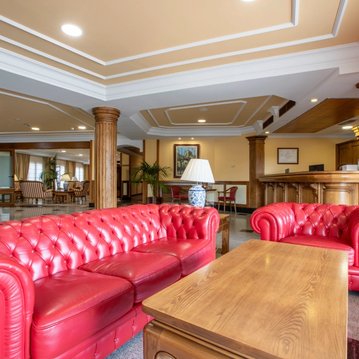 Sala elegante con sof&aacute;s rojos y mesas de madera en la recepci&oacute;n de un hotel.