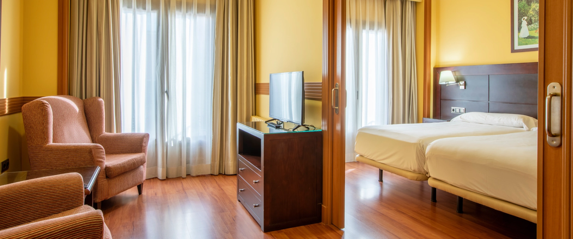 Habitaci&oacute;n de hotel con sill&oacute;n, televisor y dos camas individuales.