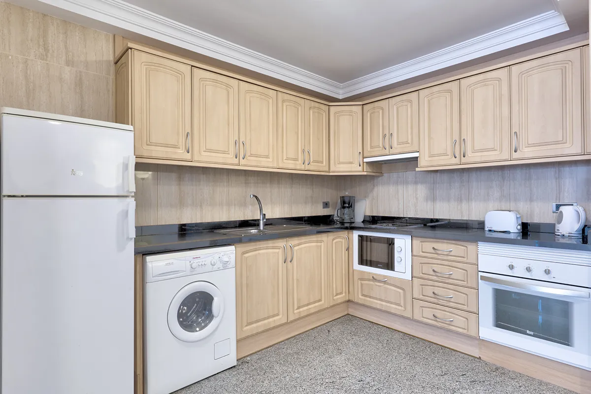 Cocina moderna con muebles de madera, electrodomésticos blancos y encimeras negras.
