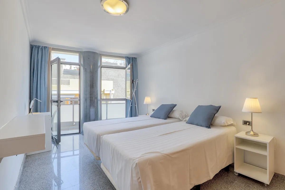 Habitación con dos camas individuales, lámparas y cortinas azul claro.