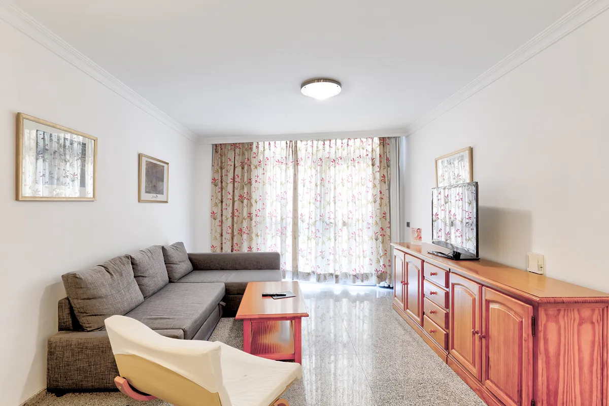 Sala de estar con sofá gris, mueble, televisión y cortinas florales.