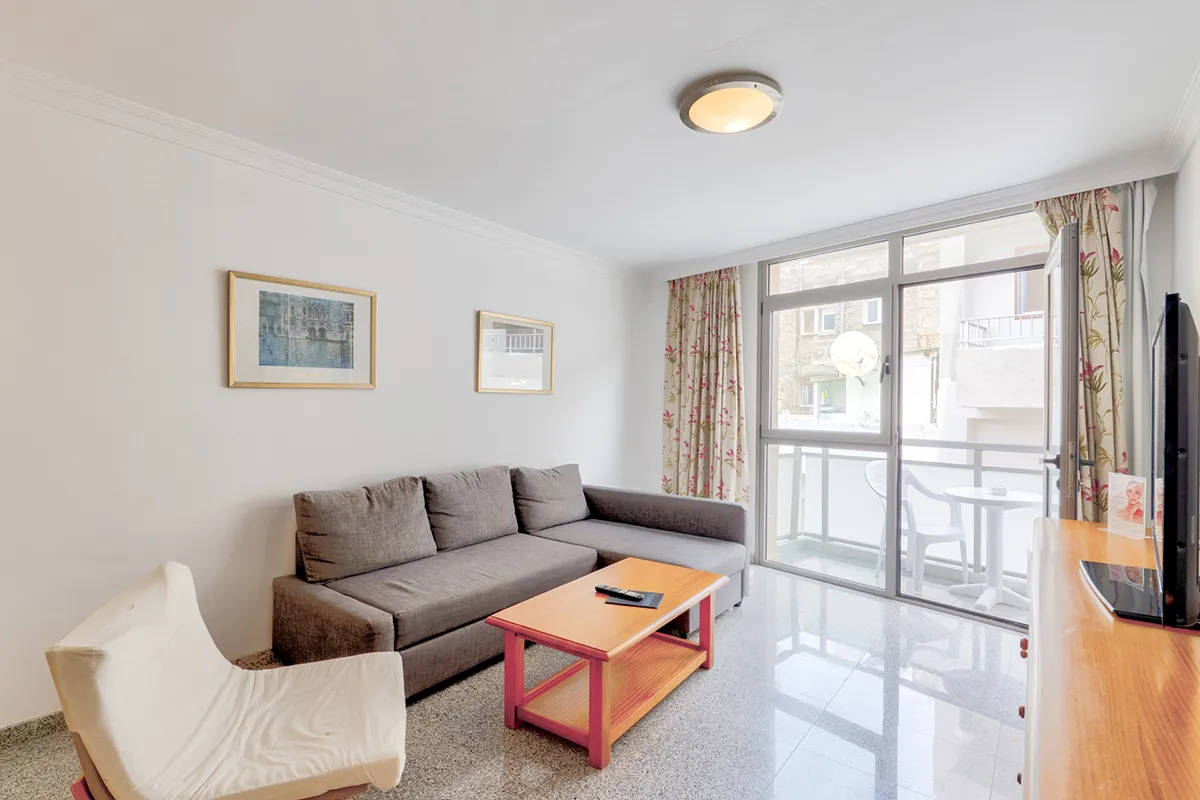 Sala de estar luminosa con sofá, mesa y balcón con cortinas floreadas.