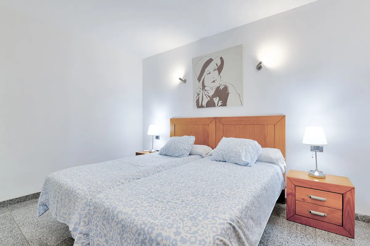 Cama doble con cabecera de madera y lámparas en un cuarto minimalista.