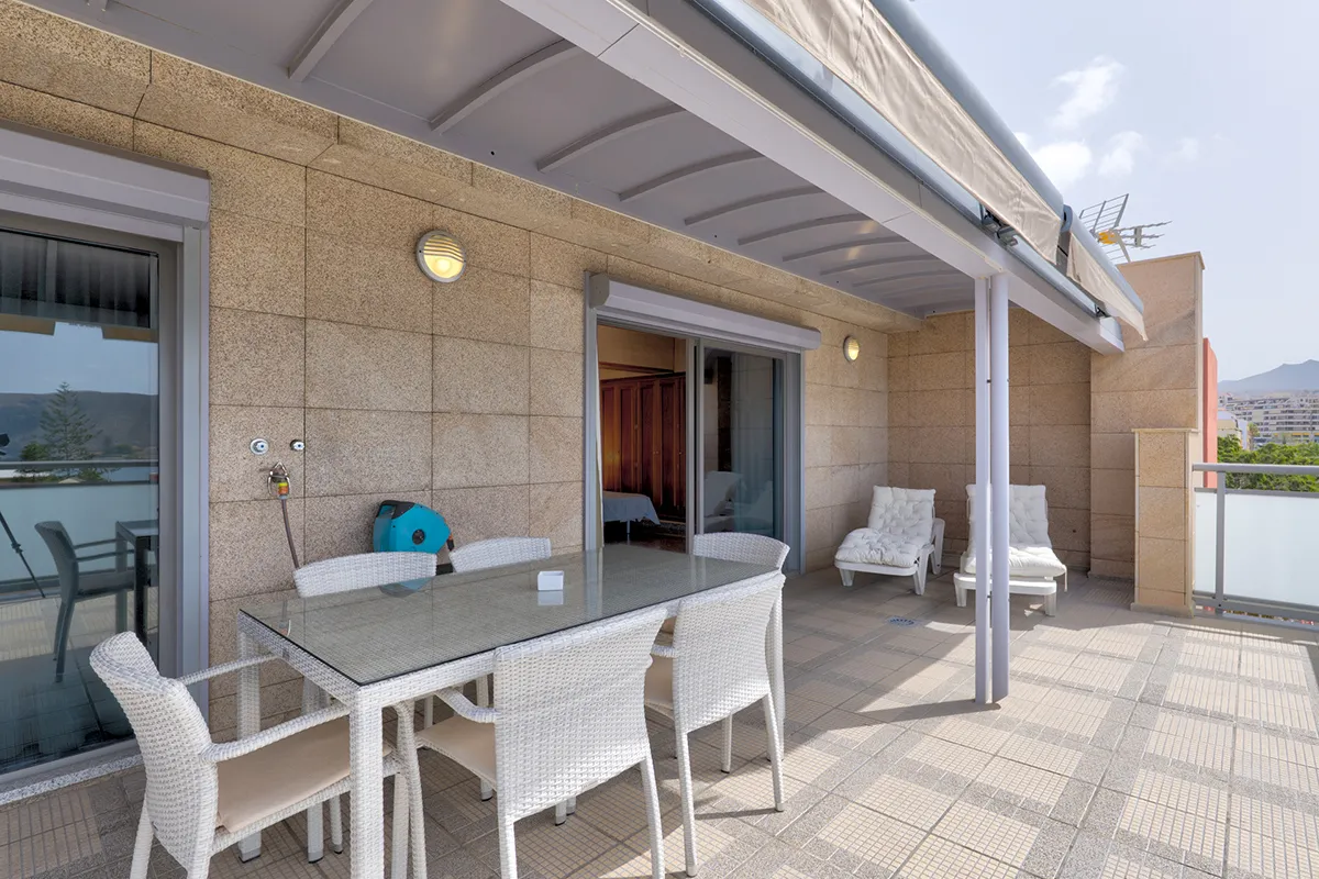 Terraza amueblada con mesa, sillas y dos tumbonas bajo techo parcial.