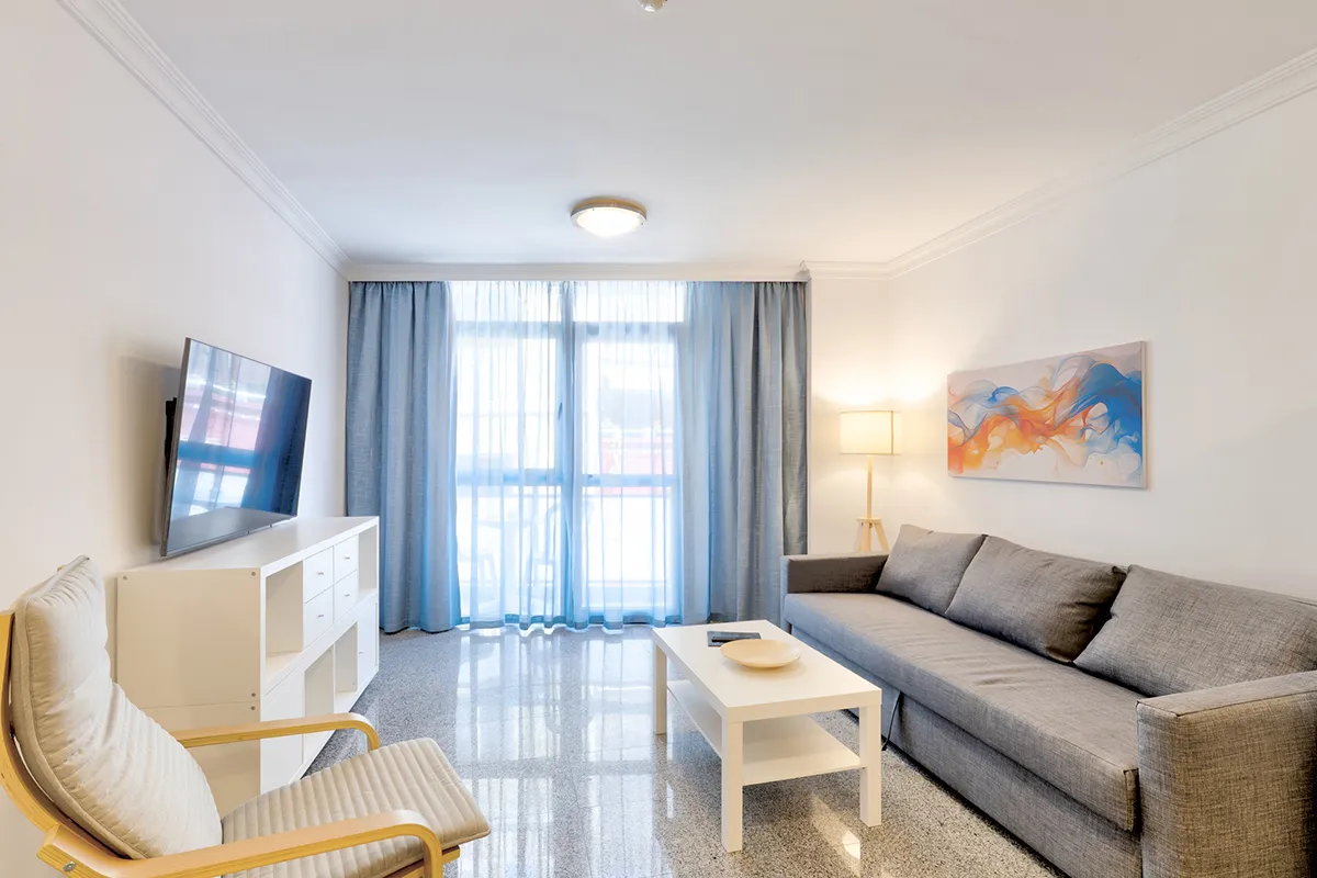 Sala moderna con sofá gris, televisor y mesa blanca.