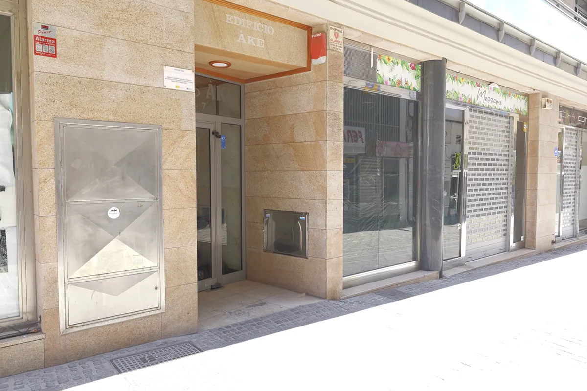 Entrada a un edificio de fachada de piedra junto a un local con persiana cerrada.