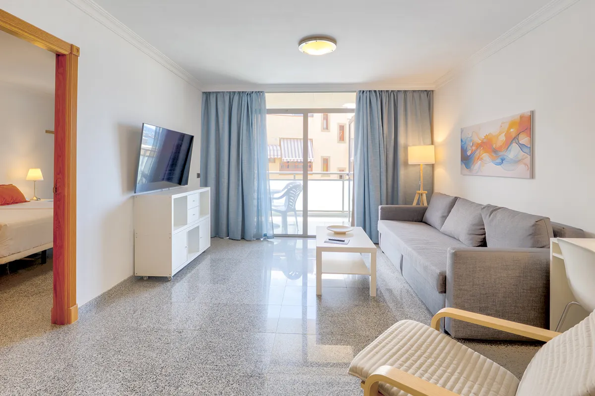 Sala moderna con sofá gris y televisor, cortinas azules y arte en la pared.