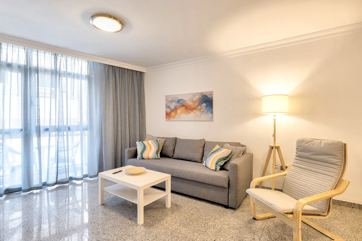 Sala moderna con sofá, silla, mesa blanca, lámpara y cortinas azules.