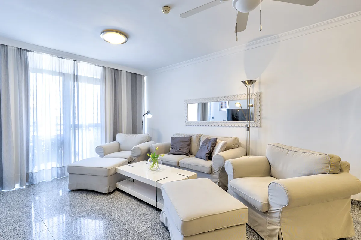 Sala con sofás beige, mesa blanca y cortinas traslúcidas.