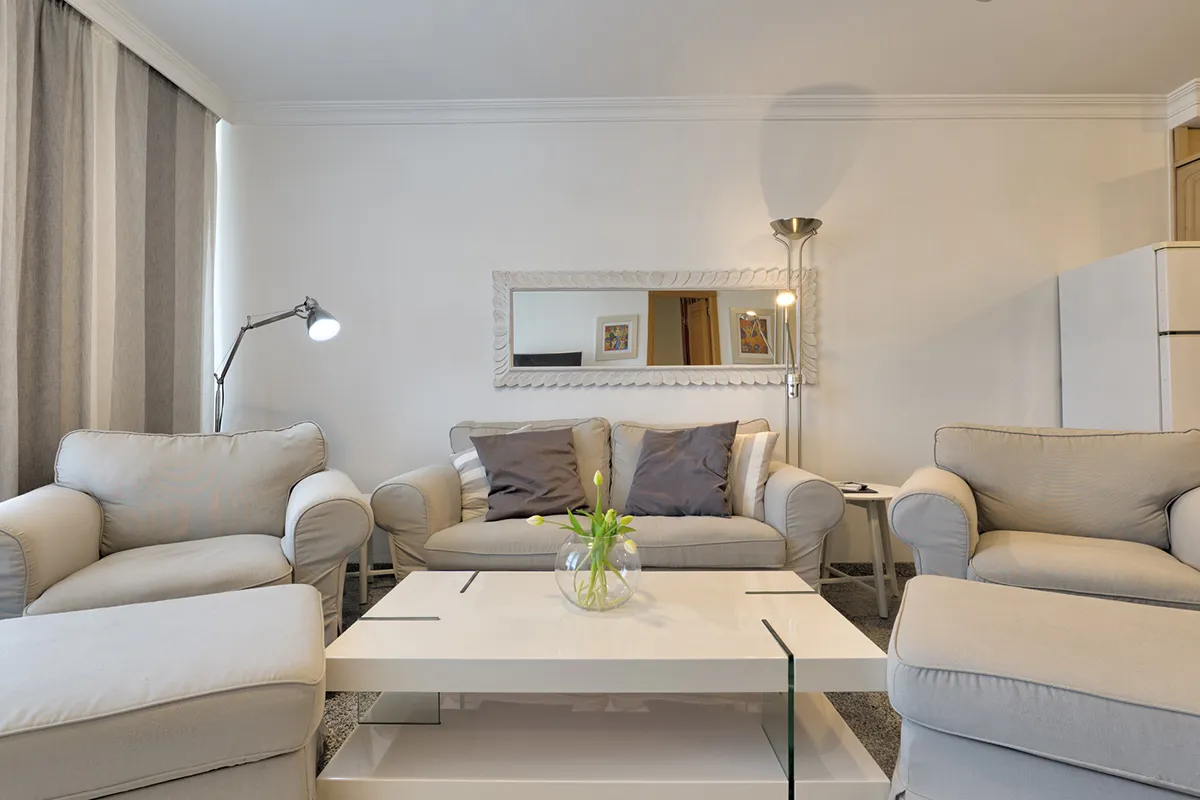 Sala moderna con sofás claros, mesa blanca y lámparas de pie.