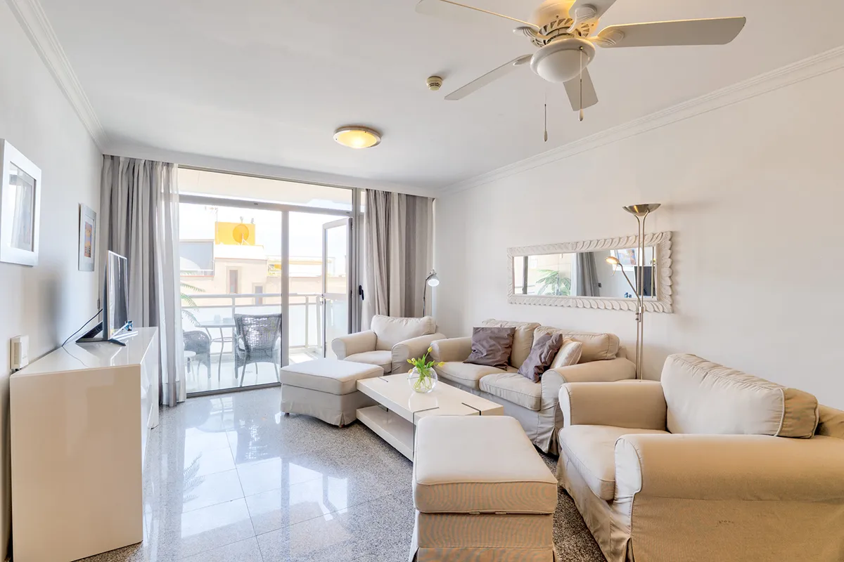 Sala luminosa con sofás beige, mesa de centro y acceso a balcón.