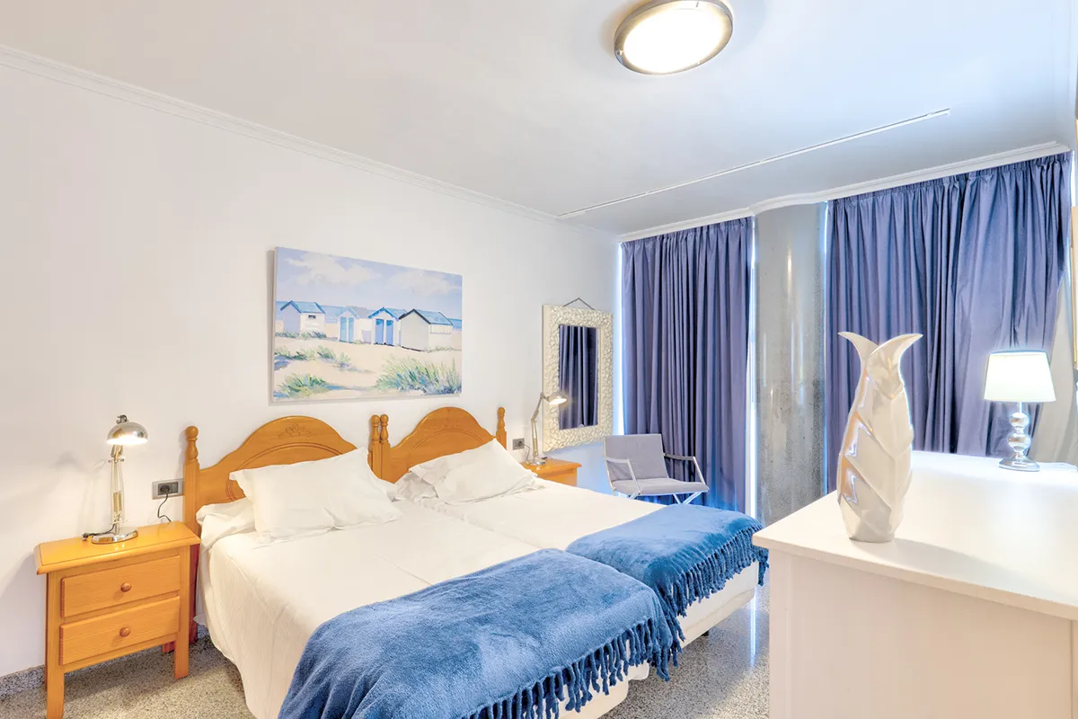 Habitación luminosa con dos camas, decoración azul y lámparas modernas.