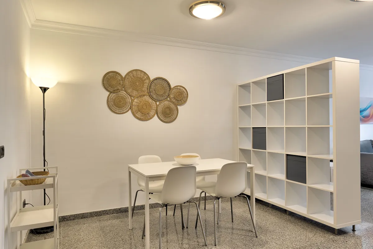 Comedor minimalista con mesa blanca y sillas, decoración de pared tejida.