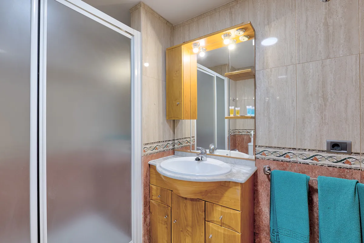 Baño con ducha, lavabo y toallas turquesas.