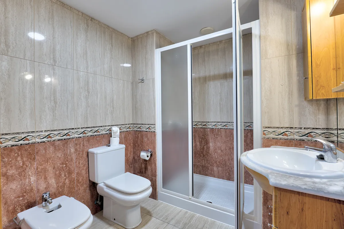 Baño con ducha, inodoro, bidé y lavabo, decorado con azulejos beige y marrón.