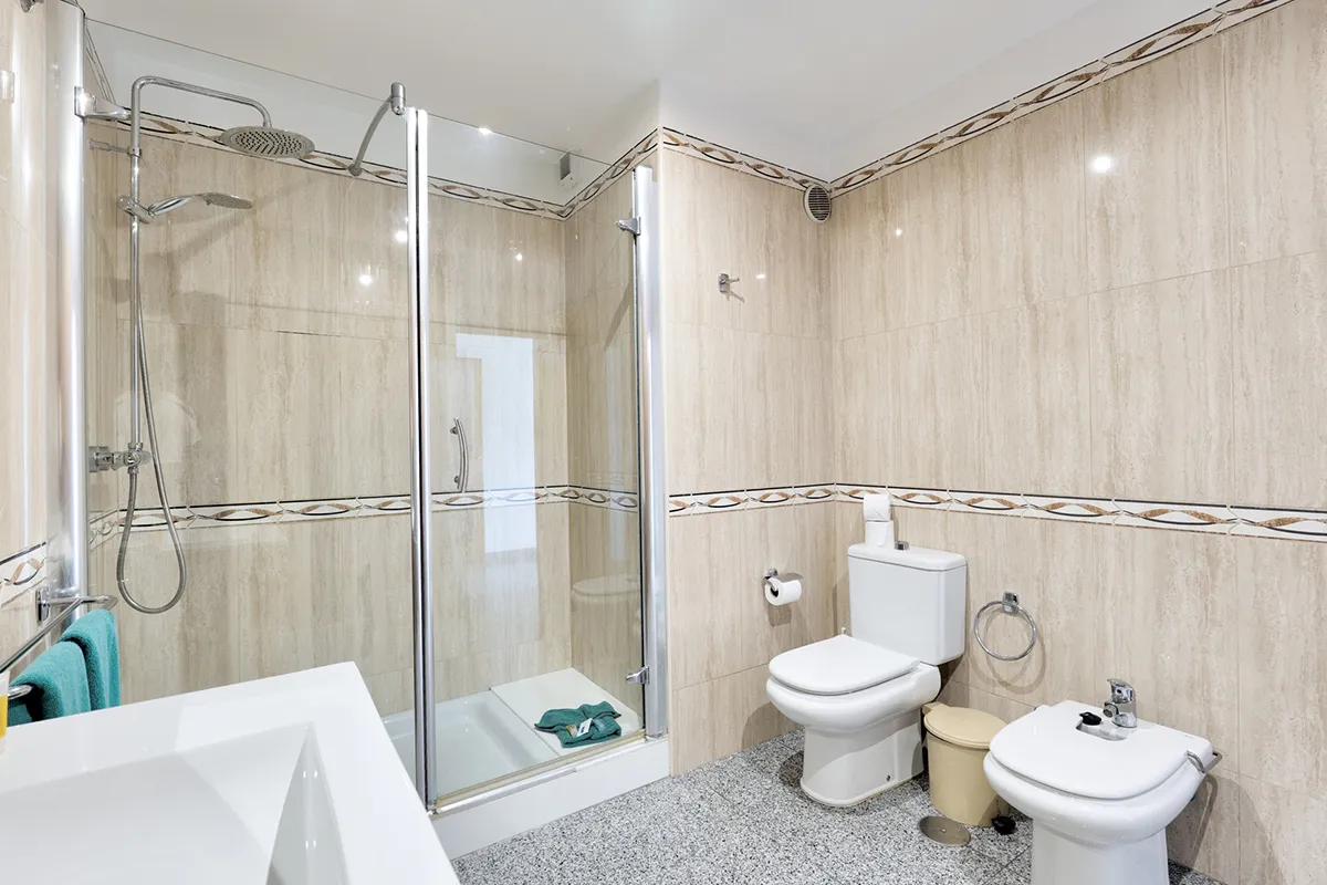 Baño moderno con ducha, inodoro, bidé y lavabo sobre suelo de mármol gris.