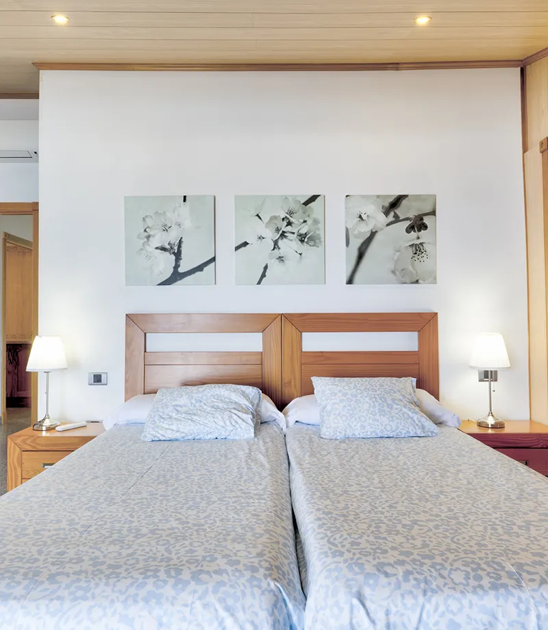 Dos camas con ropa de cama azul y cuadros de flores sobre el cabecero.