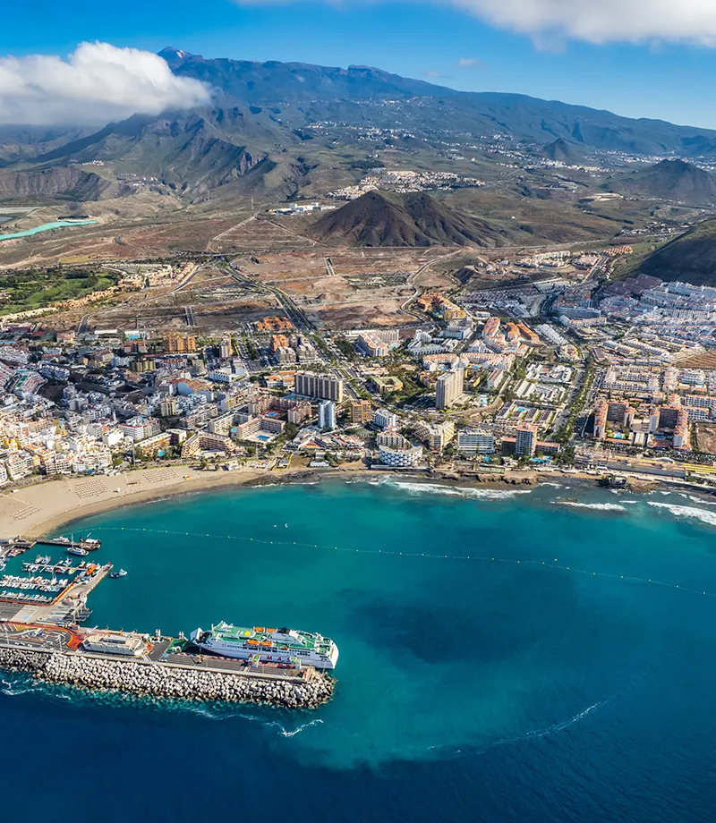 Vista a&eacute;rea de un puerto tur&iacute;stico con monta&ntilde;as al fondo.