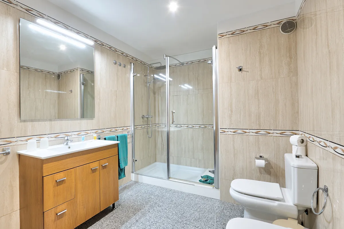 Baño moderno con ducha de cristal, lavabo, espejo y sanitarios blancos.