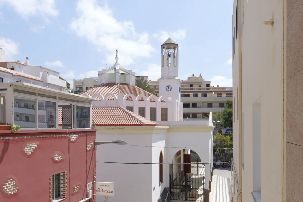 Iglesia blanca con torre y reloj, rodeada de edificios urbanos.