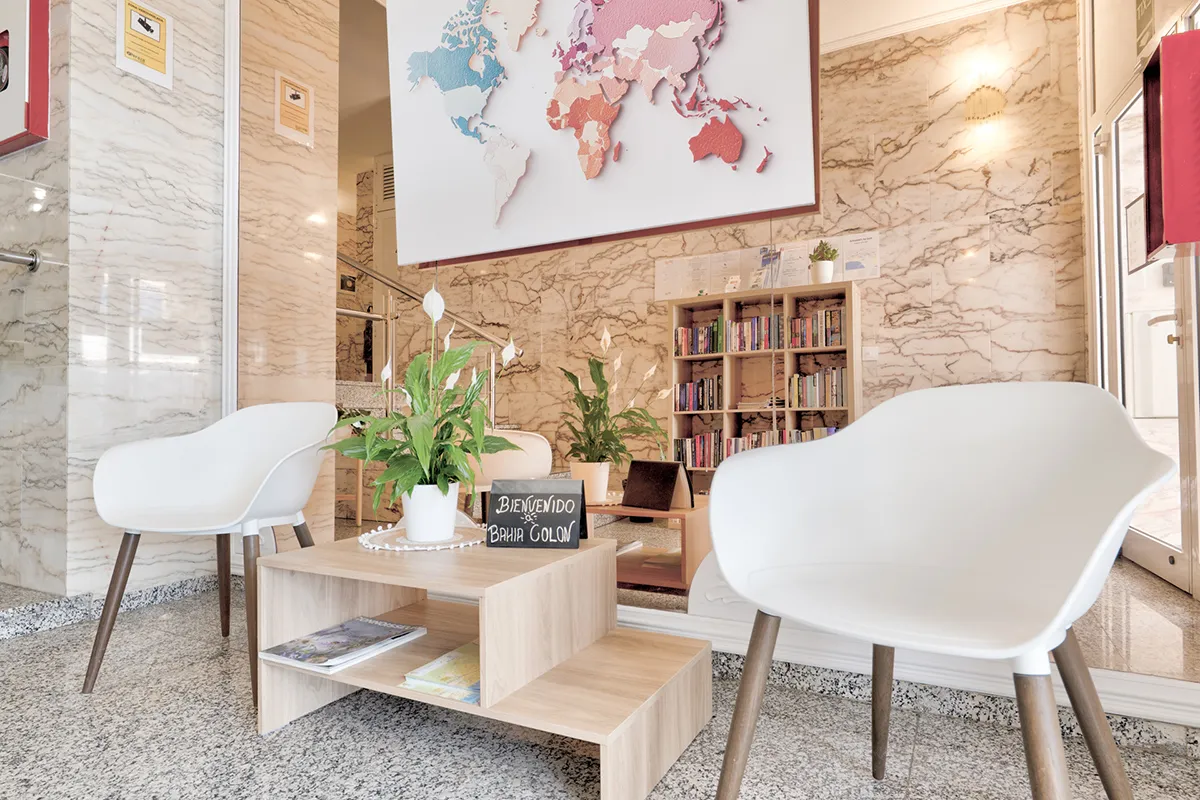 Sala acogedora con sillas blancas, plantas, un mapa y estantería de libros.