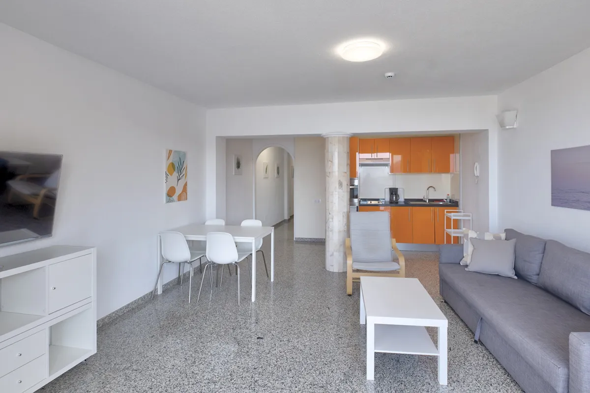 Sala amplia con cocina naranja, sofá gris y mesa blanca.