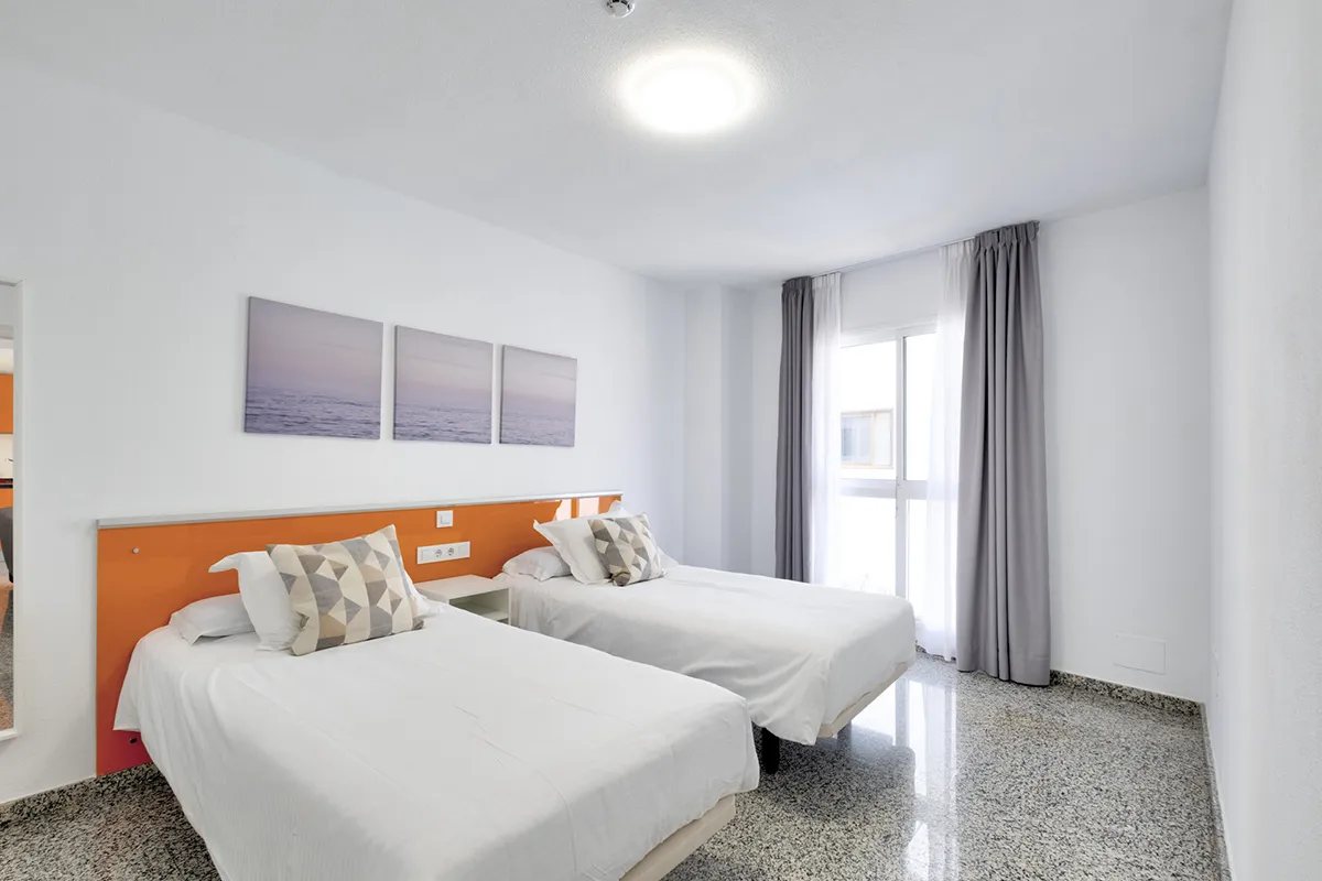 Habitación con dos camas individuales, paredes blancas y cortinas grises.