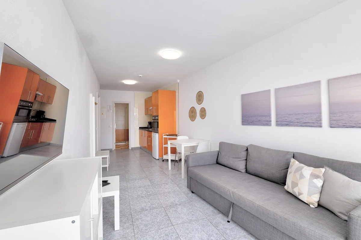 Sala moderna con cocina naranja y sofá gris.