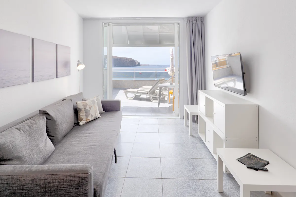 Sala moderna con sofá gris y vista al mar desde un balcón.